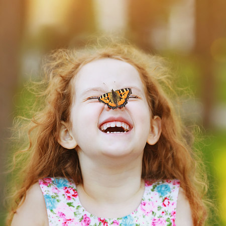 Funny laughing curly girl with a butterfly on his nose. Healthy smile with white teeth. Free breathing concept.